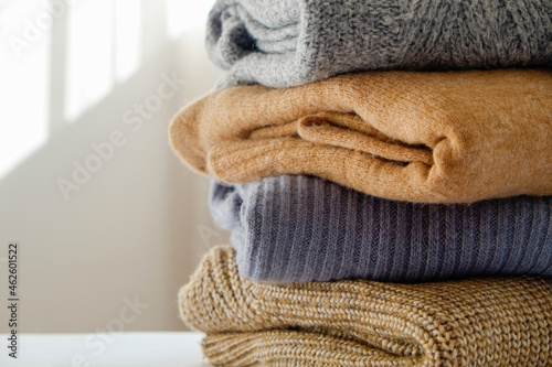 Bunch of knitted warm pastel color sweaters with different knitting patterns folded in stack, clearly visible texture. Stylish fall-winter season knitwear clothing. Close up, copy space for text.