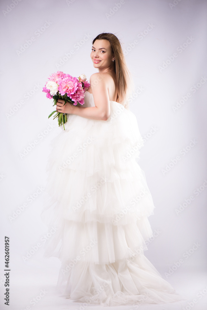 Beautiful cheerful young blonde girl wearing dress standing isolated over white background, holding bouquet of peonies Beautiful cheerful young blonde girl wearing dress standing isolated over white background, holding bouquet of peonies