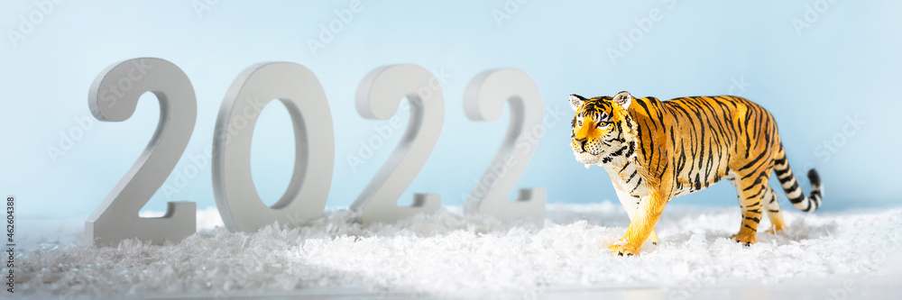Obraz premium Happy New Year 2022. Decorative white number 2022 and figurine of tiger isolated on blue background. Christmas greeting card. Banner