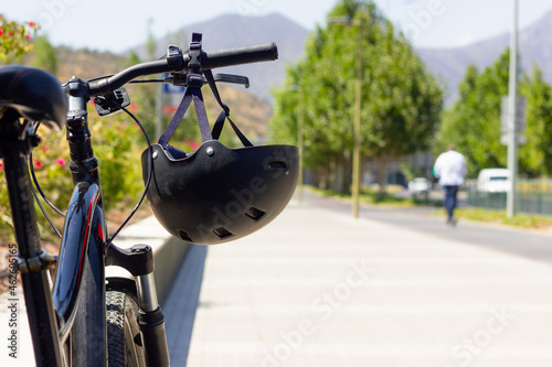 Black helmet on bicycle handlebars on street on sunny day. Safety concept