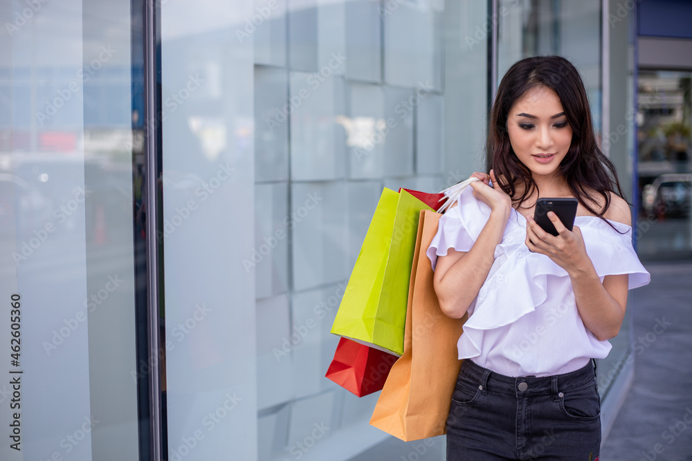 Portrait Asian beautiful happy young woman smiling cheerful and she using smartphone paymetn for shopping online with shopping bags Portrait Asian beautiful happy young woman smiling cheerful and she using smartphone paymetn for shopping online with shopping bags
