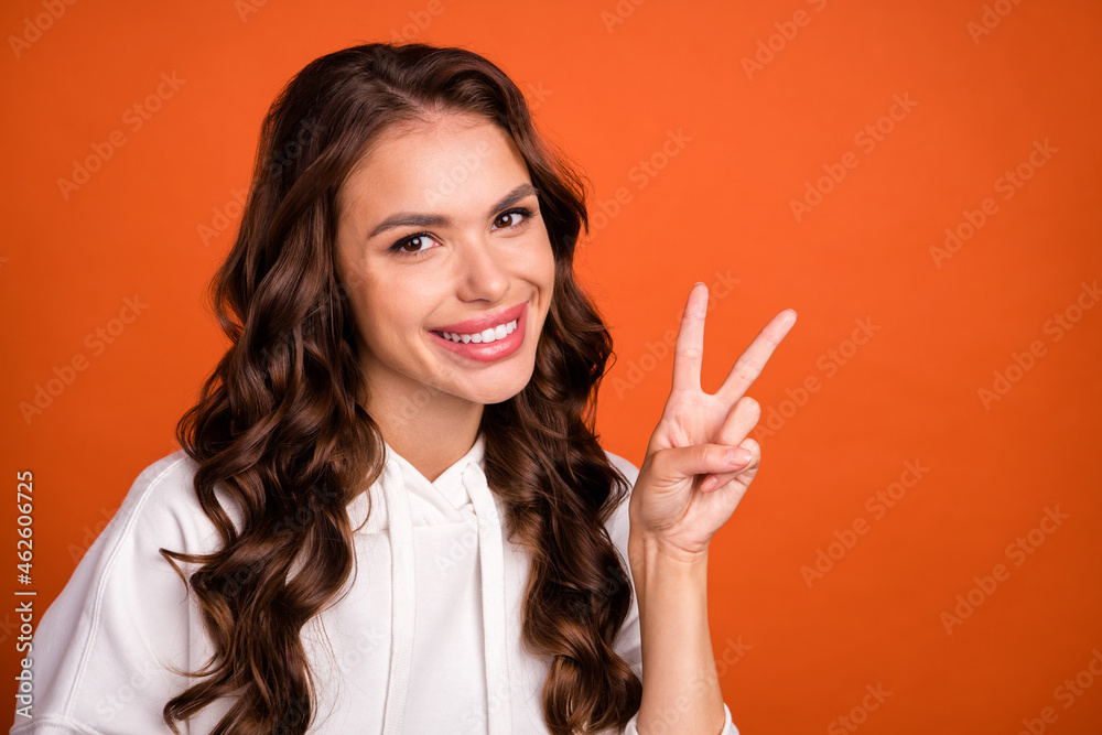 Photo portrait woman in casual outfit with long wavy hair showing v-sign gesture isolated vivid orange color background Photo portrait woman in casual outfit with long wavy hair showing v-sign gesture isolated vivid orange color background