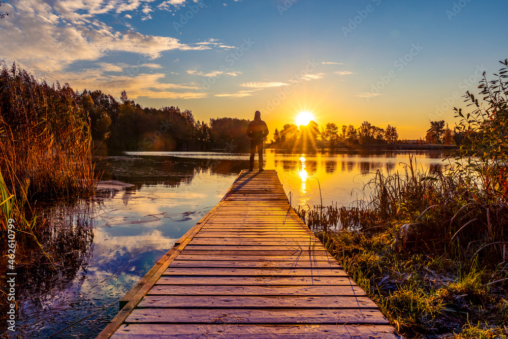 Silhouette of man standing on the lake wooden bridge facing to the sunrise