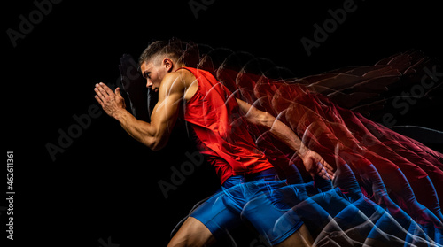 Cropped portrait of young athletic man, professional runner training isolated over black background. Stroboscope effect. photo