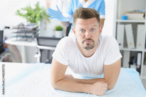 Fotografia Young sad man lying on couch in front of doctor proctologist in clinic
