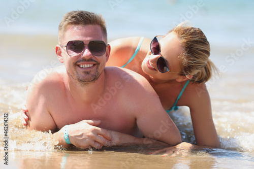 Young happy man and woman in sunglasses lying on seashore
