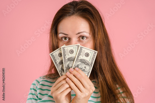 A beautiful brunette woman in casual clothes won a small amount of money in a lottery. Portrait of a girl with dollar bills covering her face