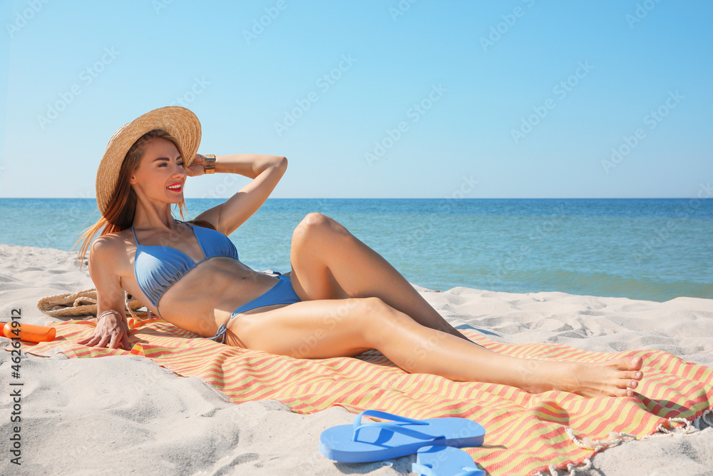 Woman with towel and other beach stuff on sand near sea Woman with towel and other beach stuff on sand near sea