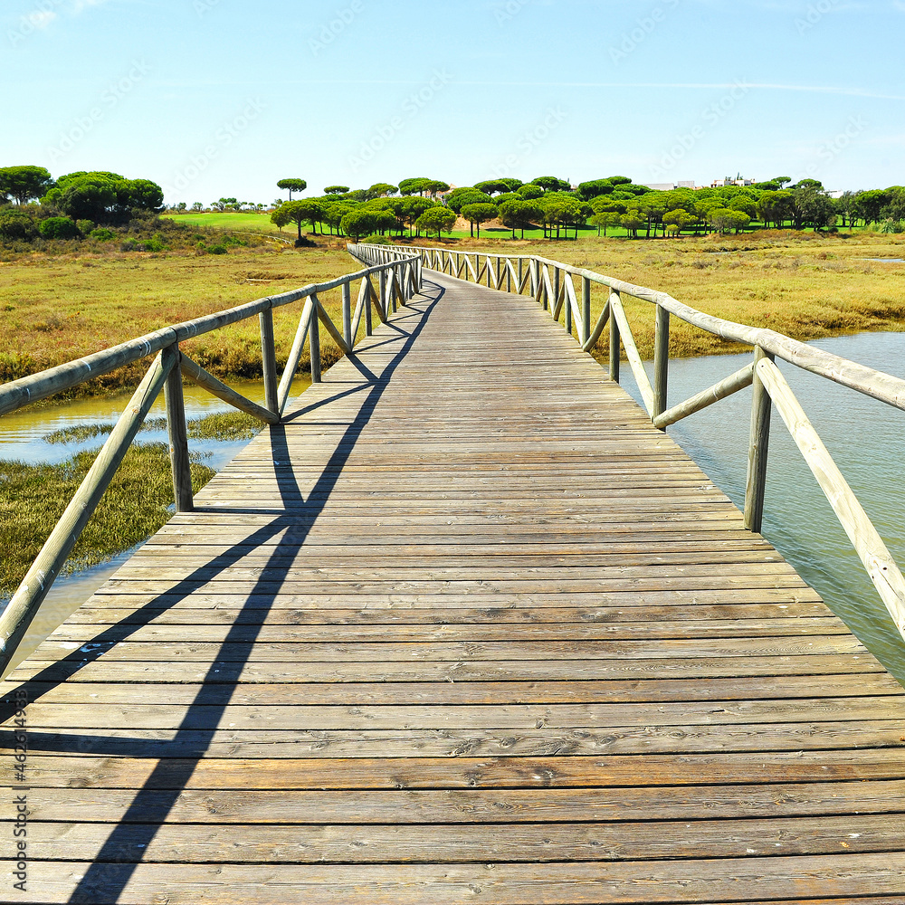 Wooden walkway in Marshes of Rio Piedras (River Stones) Natural Park in El Rompido, province of Huelva, Andalusia, Spain Wooden walkway in Marshes of Rio Piedras (River Stones) Natural Park in El Rompido, province of Huelva, Andalusia, Spain