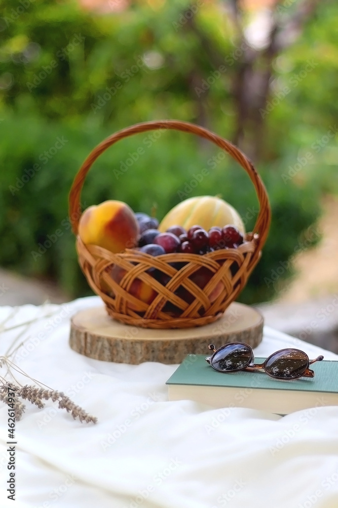 Vintage basket with various fruit, book, sunglasses and lavender flowers on a picnic basket. Selective focus.