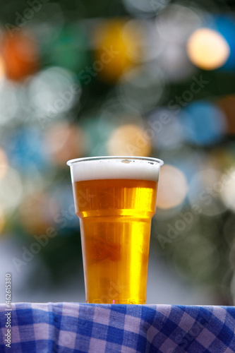 Plastic glass of beer on table with checkered tablecloth.