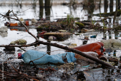 Big plastic bottles and other garbage lies on the shore of pond