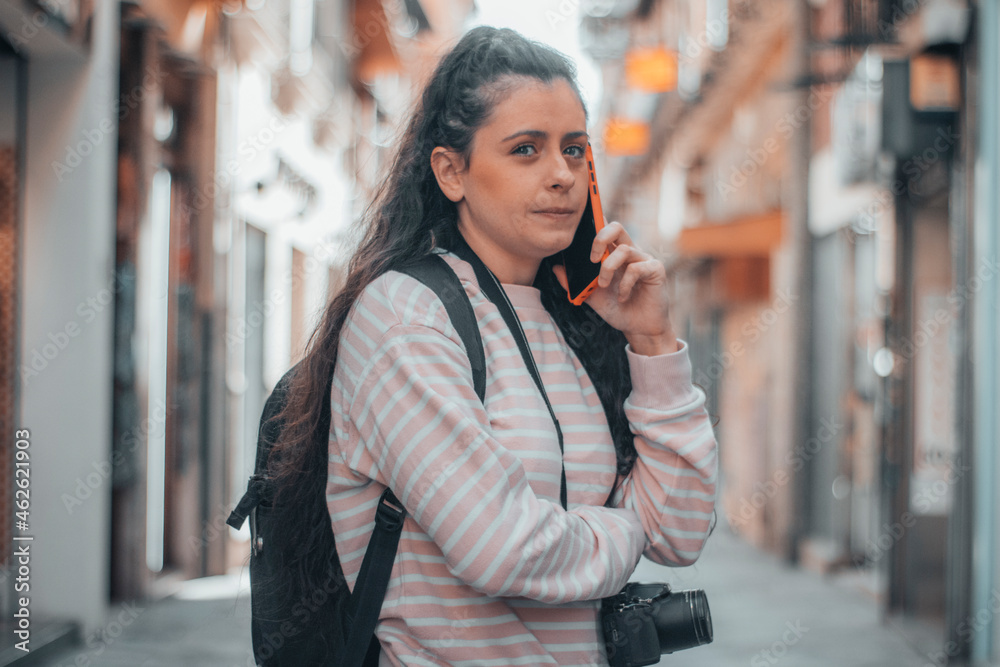 Mujer adolescente trotamundos visitando la ciudad de Marrakech llamando por teléfono mientras está viajando de ruta con su equipaje y mochila para realizar fotografías con su cámara fotográfica Mujer adolescente trotamundos visitando la ciudad de Marrakech llamando por teléfono mientras está viajando de ruta con su equipaje y mochila para realizar fotografías con su cámara fotográfica