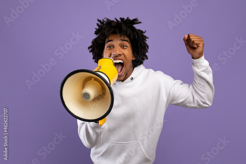 фотографія Agitated black teenager shouting into megaphone over violet studio background