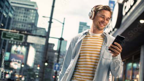 Portrait of a Beautiful Japanese Female Casually Walking on the Street, Listening to Music on Headphones from Smartphone. She Uses Phone in Big City Messaging People Online and Browsing Internet. photo