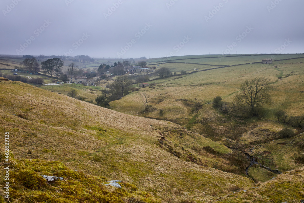 Hazy and gloomy image of upland hamlet of Moorhouses with grass covered spoil heaps and Gill Beck in the foreground
