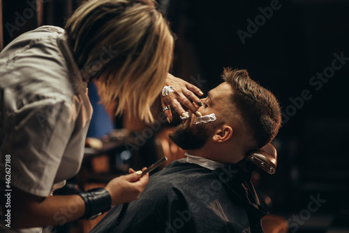 Man getting shaved with straight edge razor by hairdresser at barbershop
