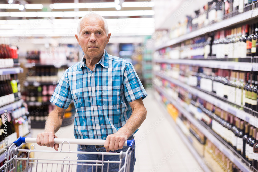 elderly retired senor buying wine in the alcohol section of the supermarket