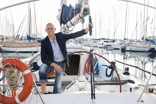 European man in jeans and a jacket posing on yacht in port