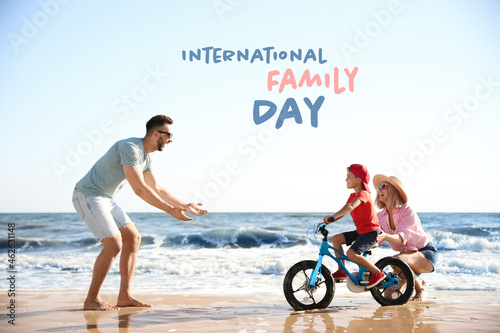 Happy parents teaching son to ride bicycle on sandy beach near sea. Happy Family Day