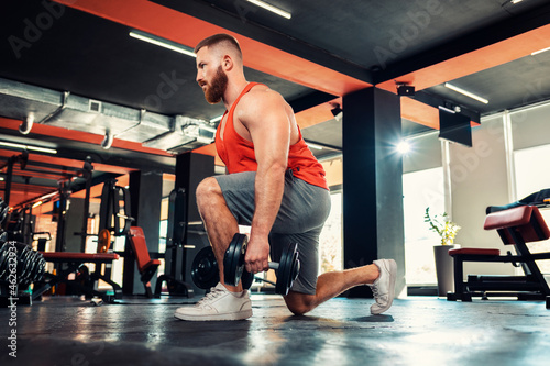 A young bearded athletic man trains with dumbbells in the gym. Squat exercise. Bottom view. The concept of fitness and workout