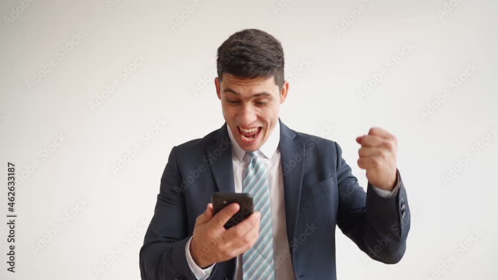 Happy male office worker in formal clothes uses mobile phone and rejoices in victory on white background. Businessman in jacket and tie experiences triumph of the winner, laughs with joy. Slow motion Happy male office worker in formal clothes uses mobile phone and rejoices in victory on white background. Businessman in jacket and tie experiences triumph of the winner, laughs with joy. Slow motion