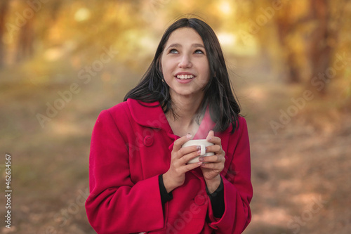 A girl in a red coat drinks tea in the autumn forest