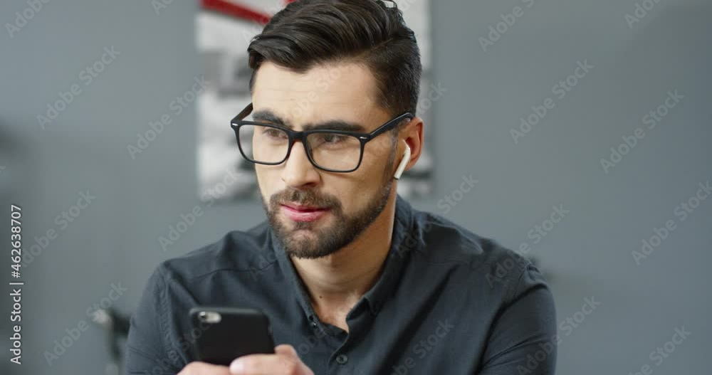 Close up of handsome caucasian successful businessman with glasses sitting in office holding smartphone looking out the window thinking over answer. Close up of handsome caucasian successful businessman with glasses sitting in office holding smartphone looking out the window thinking over answer.