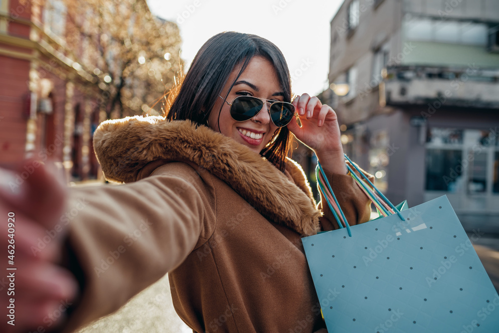 Young hispanic woman taking selfie and holding shopping bags