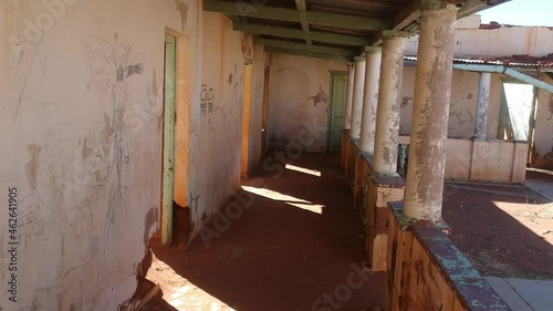 Looking down a porch of a dilapidated hotel with graffiti on the walls and no roof aerial video photo