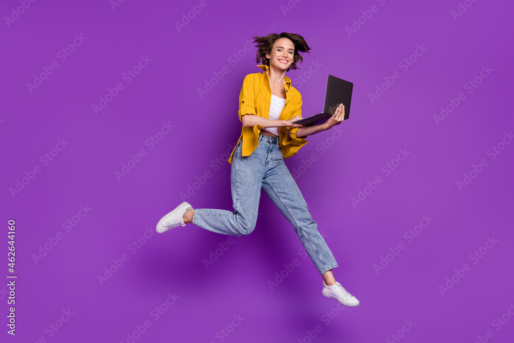 Photo of sweet charming young lady wear yellow shirt jumping high typing modern gadget smiling isolated violet color background