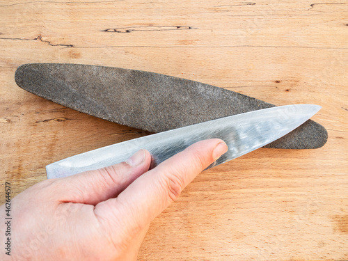 Fotografía hand sharpens kitchen knife closeup on whetstone