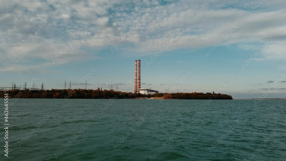 Thermal power plant on the lake shore. Striped pipes against the blue sky. You can see the forest and power lines