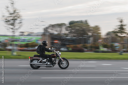 A motorcycle rides on the street at high speed. The motorcyclist is dressed in black clothes. Motion blur