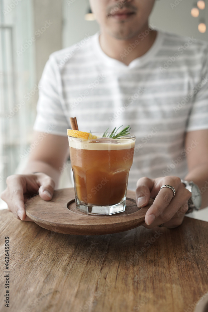 Male hands holding Nitro Orange Cold Brew garnish with rosemary on wooden table Male hands holding Nitro Orange Cold Brew garnish with rosemary on wooden table