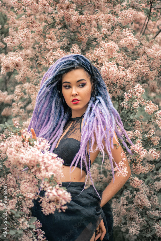 sexy young woman with color dreadlocks, in black underwear and skirt is standing under the lilac, spring fashion portrait sexy young woman with color dreadlocks, in black underwear and skirt is standing under the lilac, spring fashion portrait