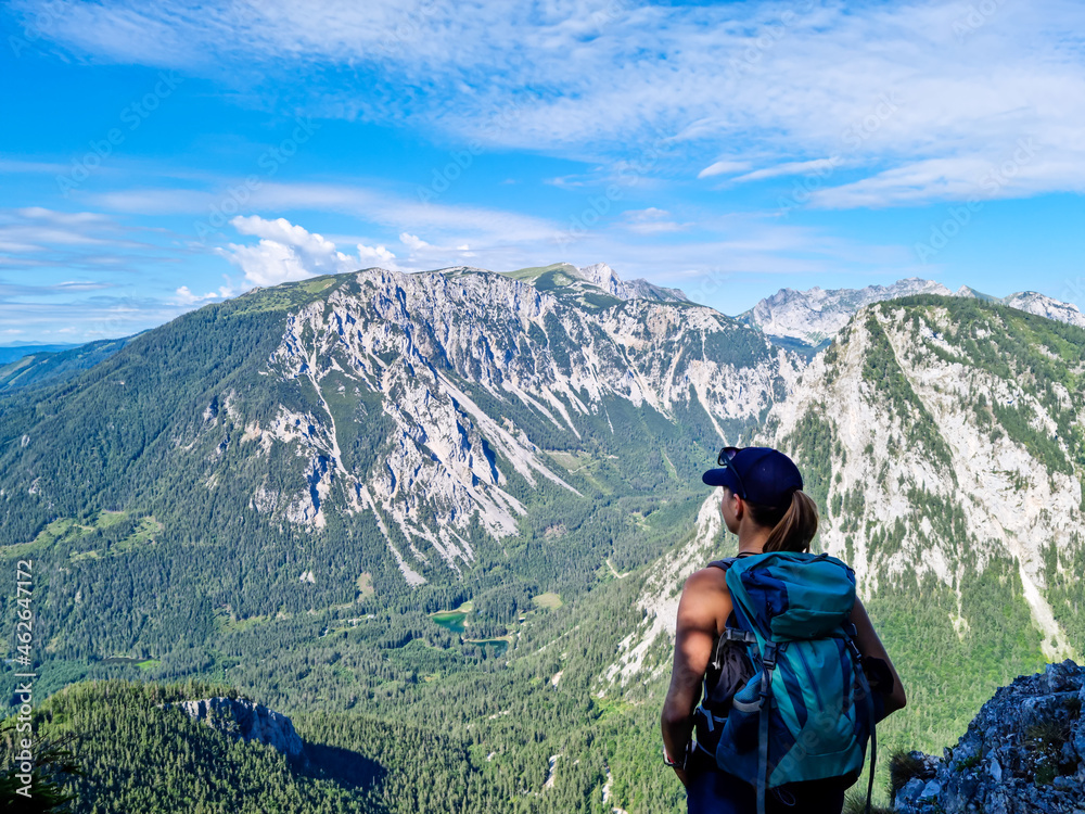 A Woman with a hiking backpack standing on the rock with a view on the Alpine mountain chains in Austria, Hochschwab region in Styria. Freedom and adventure vibes. Oberort, Tragoess