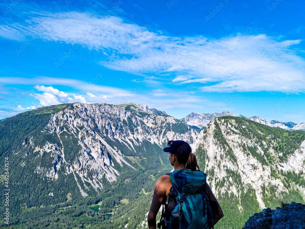 A Woman with a hiking backpack standing on the rock with a view on the Alpine mountain chains in Austria, Hochschwab region in Styria. Freedom and adventure vibes. Oberort, Tragoess