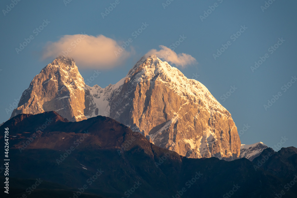First sunrise reaching the peaks of Ushba in Caucasus, Georgia. Cloudless sky above the high and snow-capped mountains. The hills below are shrouded with shadows. Daybreak. High and desolate mountains