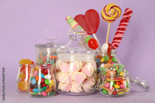 Jars with different delicious candies on violet background