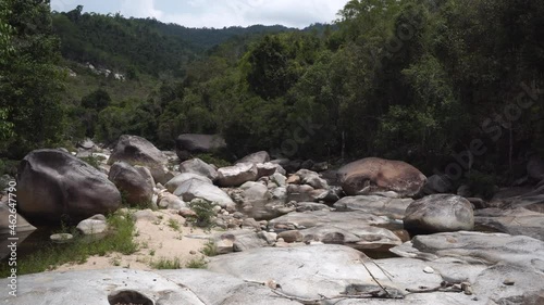 Rapids with polished stones huge pile on mountain river with narrow streams against hilly forestry bank on sunny day closeup photo