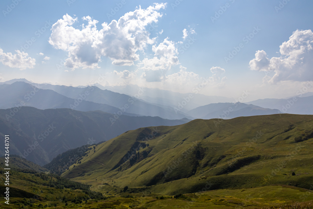 A panoramic view on high Caucasus mountains in Georgia. There are high, snowcapped peaks in the back. Lush pasture in front. Idyllic landscape. Calmness and meditation. Natural remedy. Few clouds