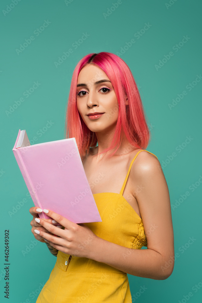 pretty young woman with pink dyed hair holding book isolated on blue