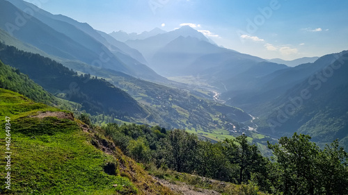 A panoramic view on Zhabeshi, a mountain village, located on the bank of the river Mulkhura in Georgia. High Caucasus mountain chains. Lush green pastures with a few cows grazing on them. Idyllic © Chris