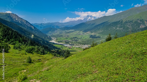 A panoramic view on Zhabeshi, a mountain village, located on the bank of the river Mulkhura in Georgia. High Caucasus mountain chains. Lush green pastures with a few cows grazing on them. Idyllic photo