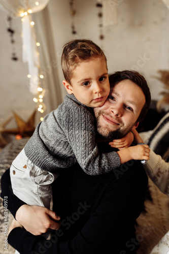 Portrait of happy father hugging with little son  looking at the camera  smiling. Loving parent spending winter holidays with his child at home  enjoying time together  fatherhood concept