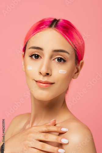 pleased young woman with dyed hair and face cream on cheeks isolated on pink