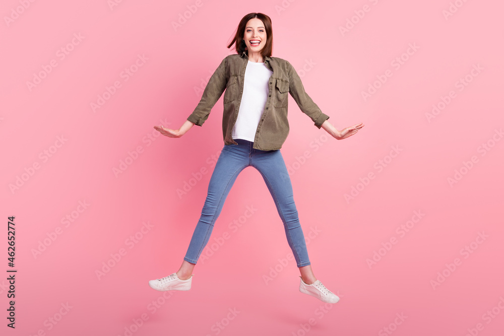 Full length photo of funny brunette hairdo lady jump wear green shirt jeans sneakers isolated on pink color background Full length photo of funny brunette hairdo lady jump wear green shirt jeans sneakers isolated on pink color background