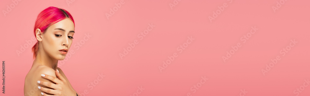 Fototapeta premium pretty young woman with colorful hair touching bare shoulder isolated on pink, banner