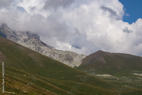 A panoramic view on high Caucasus mountains in Georgia. There are high  snowcapped peaks in the back. Lush pasture in front. Idyllic landscape. Thic clouds above the sharp peaks. Natural remedy